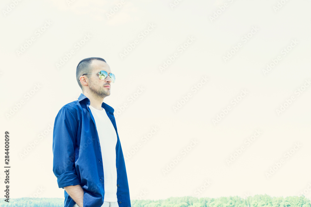 Attractive man in sunglasses stands in the Park in the summer, looks into the distance, copy space, close up, toned Attractive man in sunglasses stands in the Park in the summer, looks into the distance, copy space, close up, toned