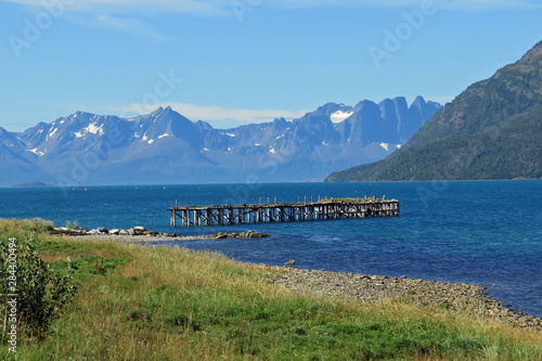 Forsaken wooden embarkment pier located in the Altafjord in front of snow covered mountains; Norway, Europe