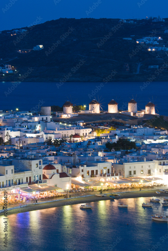 Greece, Mykonos, Hora. Night view overlooking harbor with illuminated windmills atop hillside.