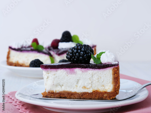 No-bake blackberry cheesecake slice with graham cracker crust, cream cheese filling and blackberry jelly, decorated with whipped cream on cake cutter over white plate.