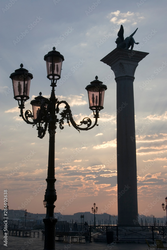 Italy, Venice. Lion of St. Mark atop column and ornate lamp at sunrise.