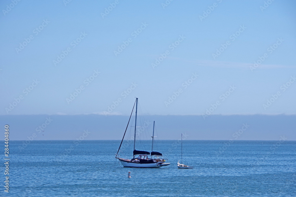 Single sailboat on the tranquil San Luis bay in California with blue sky and a wall of fog behind