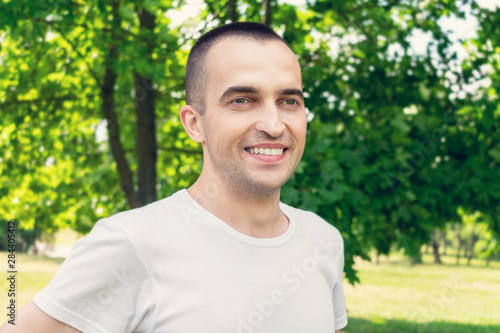 Portrait, young attractive man smiling in Park in summer, man looks into the distance, close up, toned