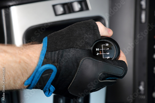 Dłoń w rękawiczce na dźwigni zmiany biegów w samochodzie osobowym, pięcio biegowym.