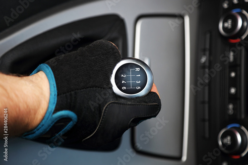 Dłoń w rękawiczce na sześcio biegowej dźwigni zmiany biegów w samochodzie osobowym.