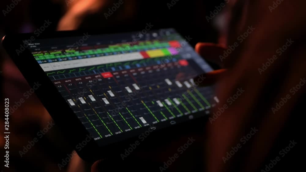 The sound engineer remotely adjusts the sound at the concert using the program on a large tablet. Control sliders settings during the performance of a musical group. Digitalization of work. Yellow The sound engineer remotely adjusts the sound at the concert using the program on a large tablet. Control sliders settings during the performance of a musical group. Digitalization of work. Yellow