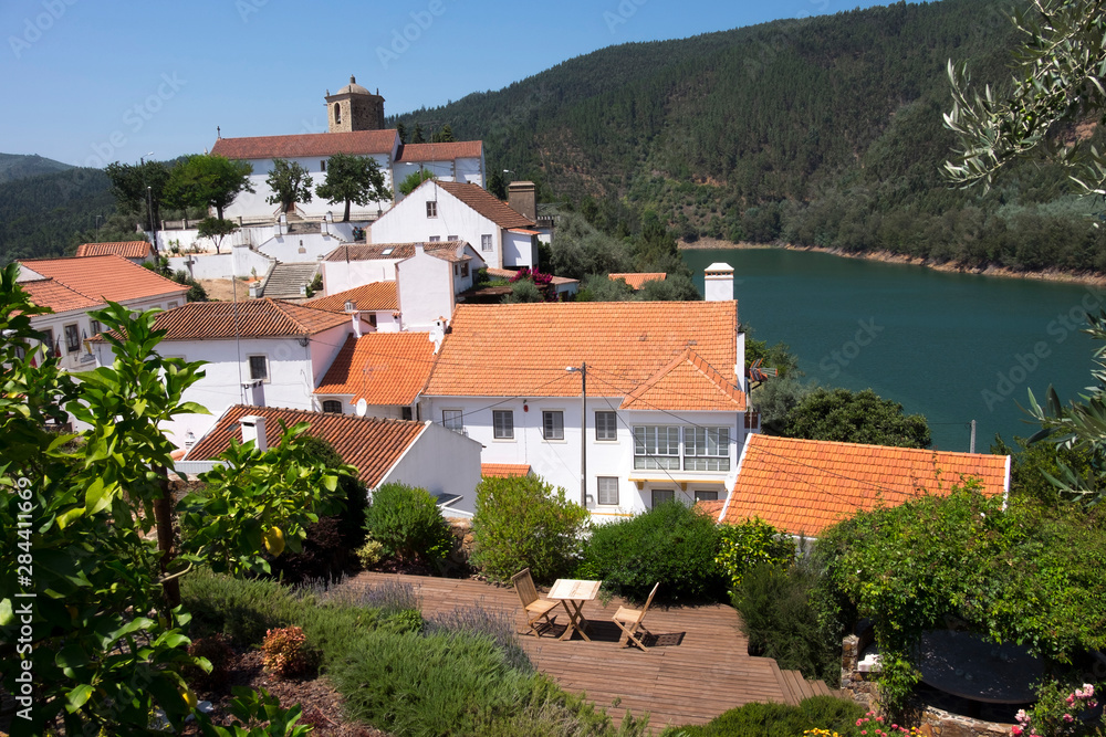Portugal, Tomar, Castelo de Bode Dam and River Zezere. Tiled roofs of village houses. Patio table with 2 chairs.