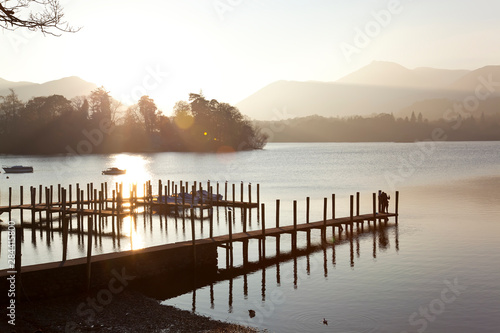 Canvas-taulu Young couple on pier, sunset, Derwent Water, Lake District, Cumbria, UK