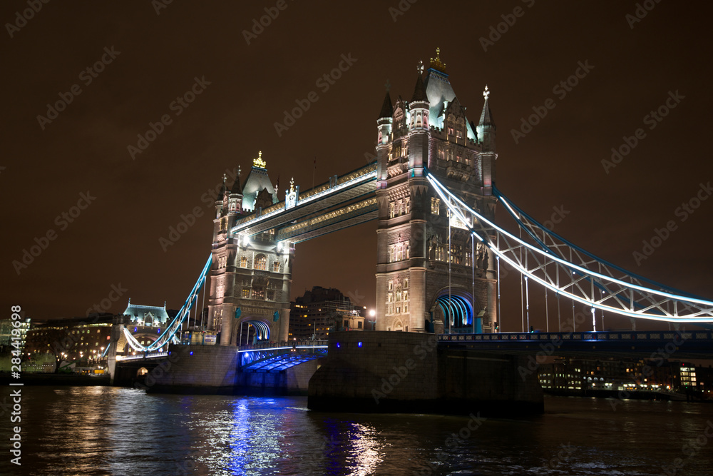 Obraz premium Tower Bridge na Tamizie, jasno oświetlony nocą, jest popularną atrakcją turystyczną Londynu.