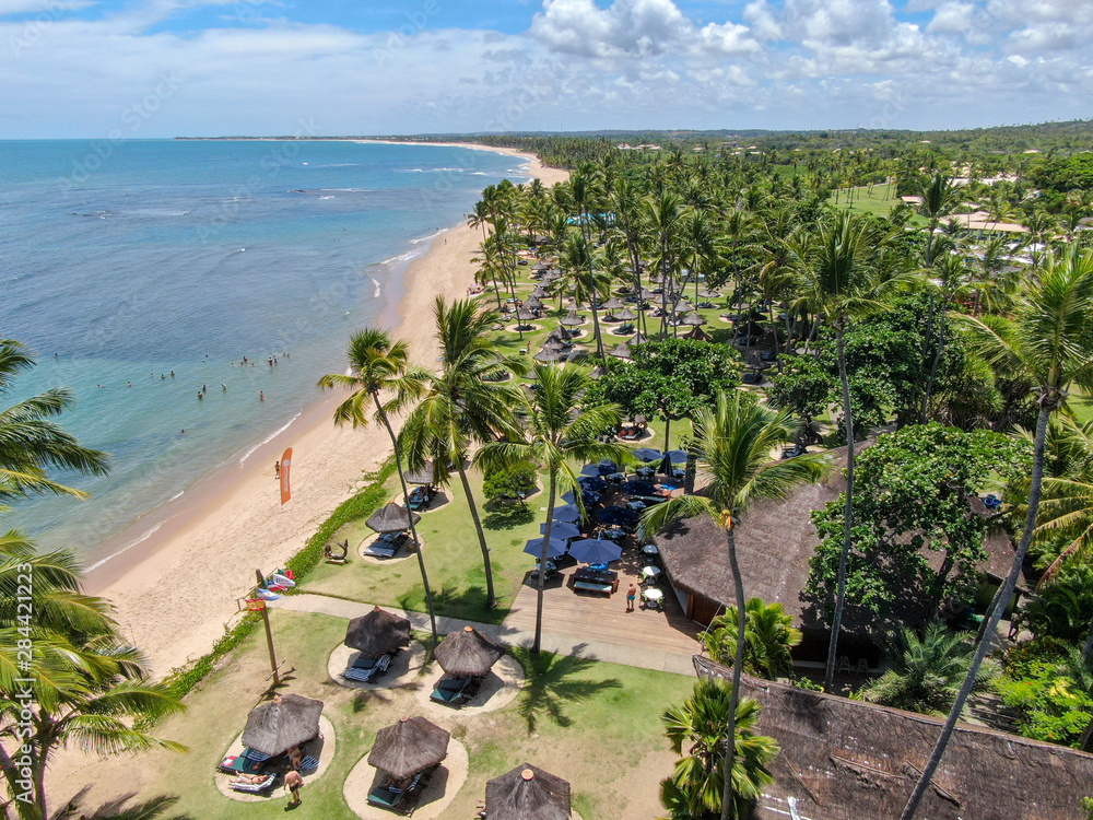 Naklejka premium Aerial view of tropical white sand beach, palm trees, umbrellas and turquoise clear sea water in Praia do Forte, Bahia, Brazil. Travel tropical destination in Brazil
