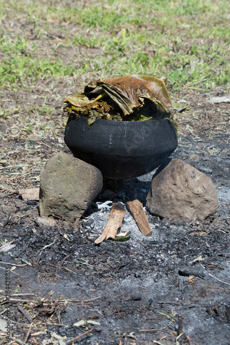 Melanesia, Papua New Guinea, Dobu Island. Typical pottery crock over open fire cooking fish and vegetables covered with palm leaves to steam the meal. photo