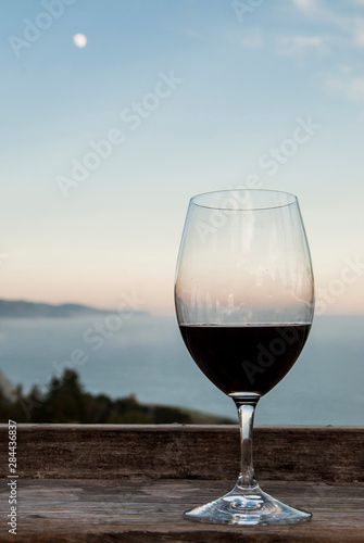USA, California, Big Sur, Nepenthe restaurant, view of Lucia Mountains, Pacific Ocean, glass of red wine and full moon