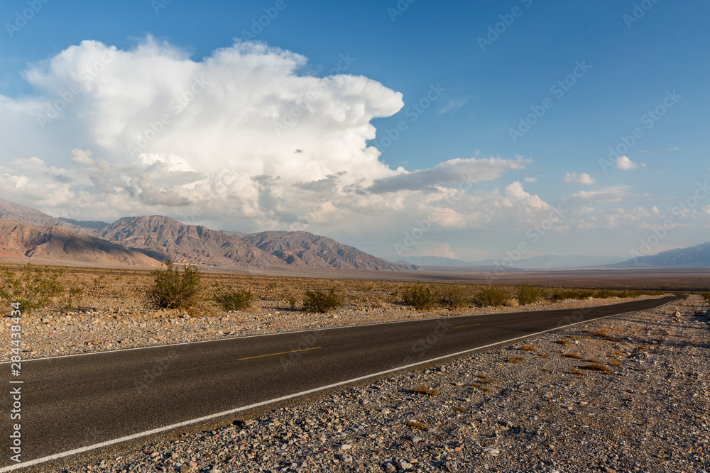 Vast open road in Death Valley National Park with afternoon clouds forming in the background