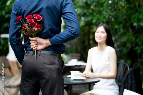 A man is proposing marriage to a smiling woman with a lovely flower bouquet in a beautiful garden, lover and couple concept, surprising proposal photo