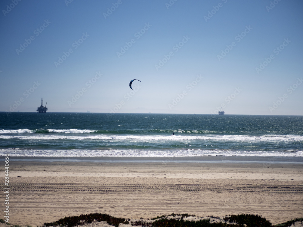 Kite surfer and oil rig at the beach.