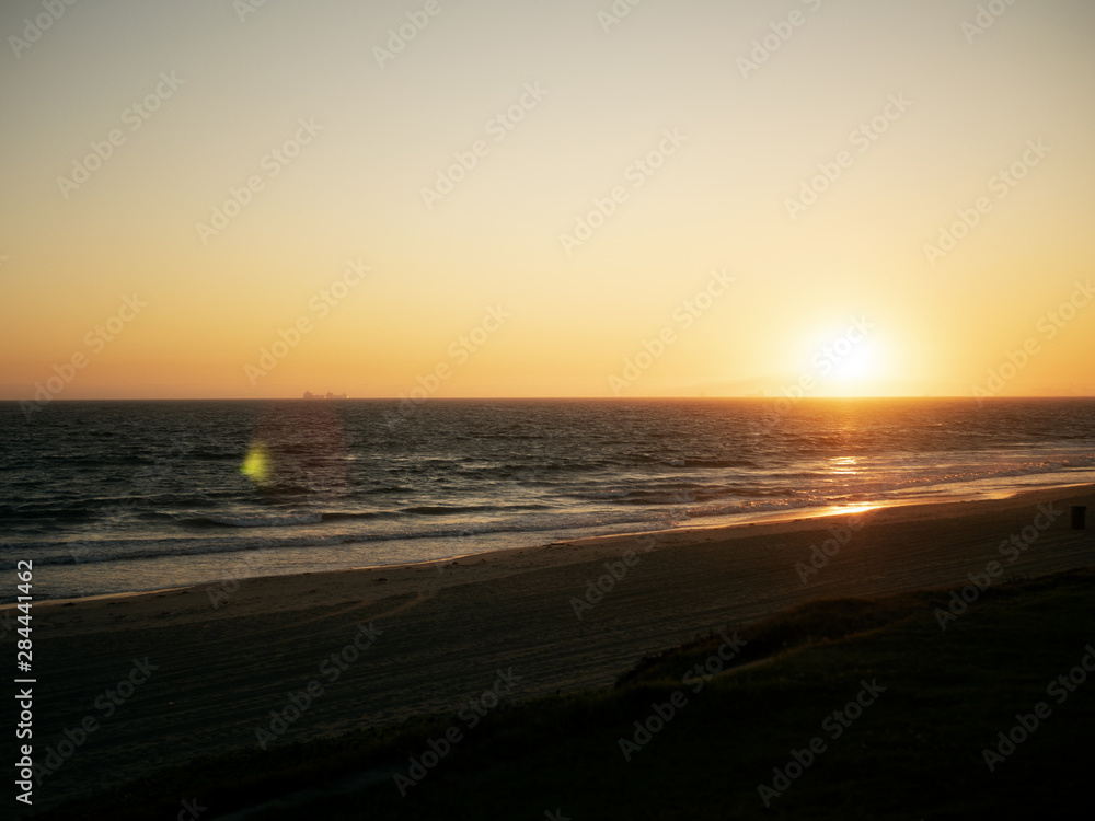 sunset with lens flare and beach in silhouette.