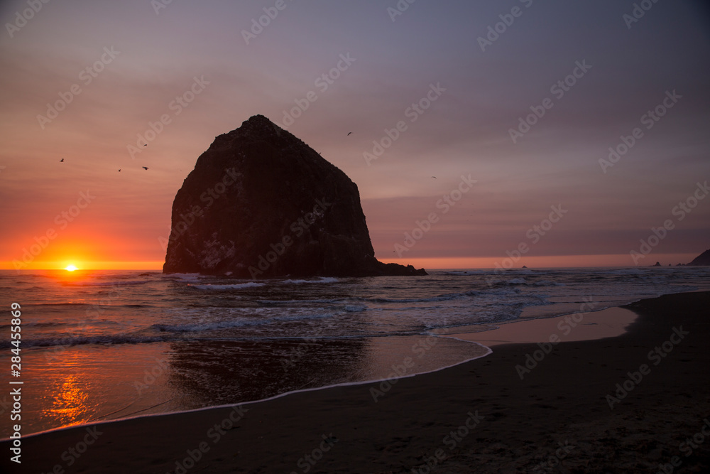 Cannon Beach, Oregon. Glowing sunset dips into the water framing the seagulls and the Haystack Mountain