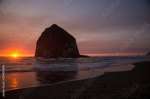 Cannon Beach, Oregon. Glowing sunset dips into the water framing the seagulls and the Haystack Mountain