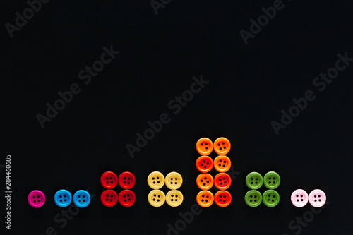 Buttons sorted by color in groups on a black background, shot from above, closeup.