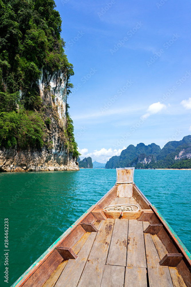 Wooden boat on green lake with limestone mountains and cliff