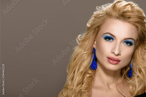 Beautiful female model with elegant hairstyle and blue earrings on cappuccino color background