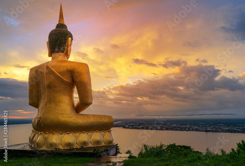 The big golden Buddha statue of Phu Salao temple with Mekong River flows through the Pakse city in beautiful sunset moment at Pakse, Laos photo