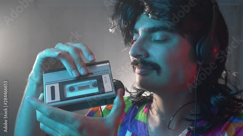 Man with mustache and mullet from the 70s 80s 90 listens to his music using a portable walkman cassette player. Vintage concept.