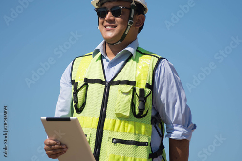 bottom rear view of male engineer walking and holding tablet computer on bright blue sky for planing a construction dress with protective vest, hard helmet and © SVRSLYIMAGES