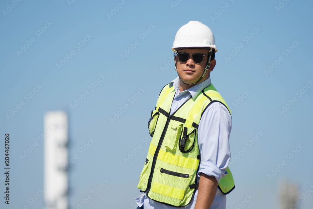 Portrait of Confident Asian engineer. Handsome young man in hardhat using glasses while standing outdoors and against blue sky Portrait of Confident Asian engineer. Handsome young man in hardhat using glasses while standing outdoors and against blue sky