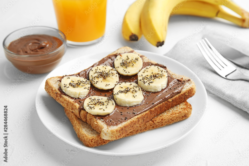 Slice of bread with chocolate paste and banana on white table