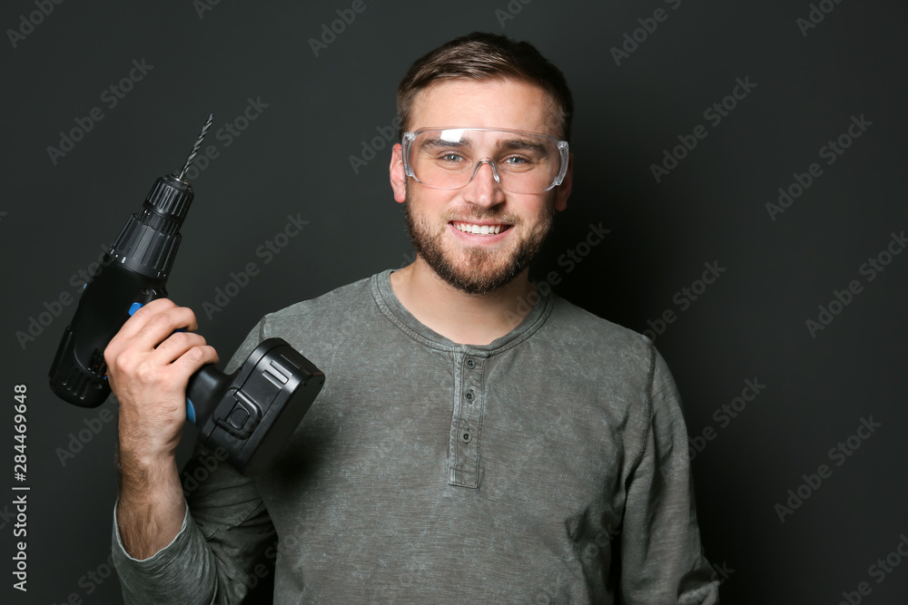 Young working man with power drill on dark background Young working man with power drill on dark background