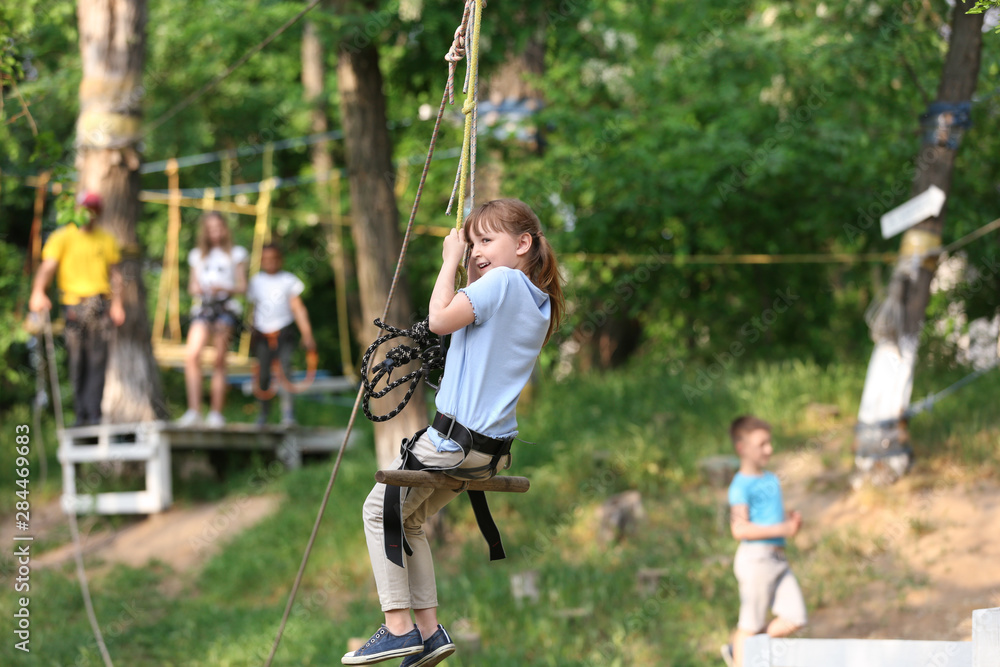 Little girl on zip line in adventure park. Summer camp