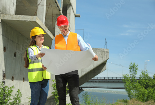 Professional engineers in safety equipment with drafting at construction site. Space for text
