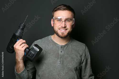 Young working man with power drill on dark background