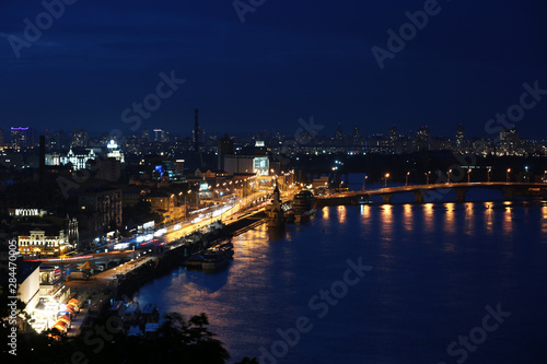 KYIV  UKRAINE - MAY 21  2019  Beautiful view of night cityscape with illuminated buildings near river and bridge