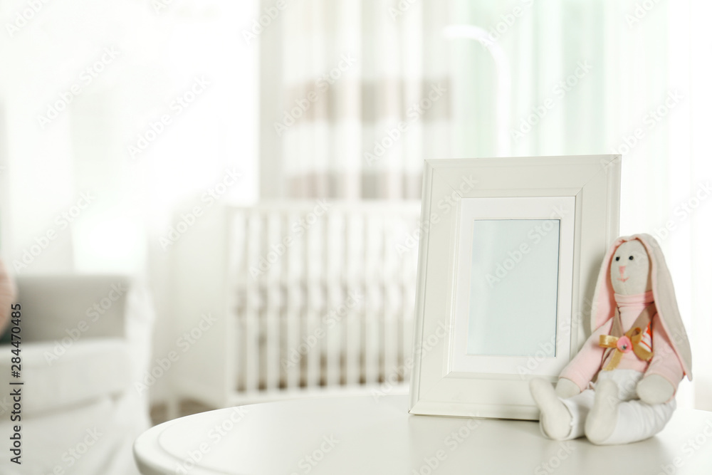 Photo frame and stuffed toy bunny on table in baby room interior. Space for text