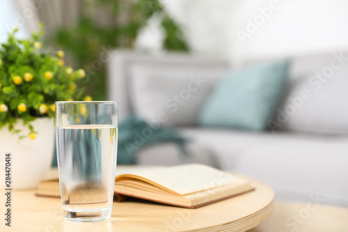 Glass of water and book on coffee table in modern living room interior. Space for text