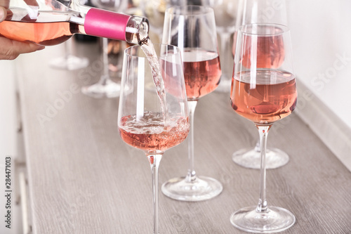 Fototapeta Naklejka Na Ścianę i Meble -  Young woman pouring delicious rose wine from bottle into glass on wooden counter, closeup
