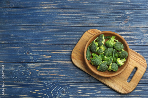 Bowl of fresh broccoli on blue wooden table, top view with space for text