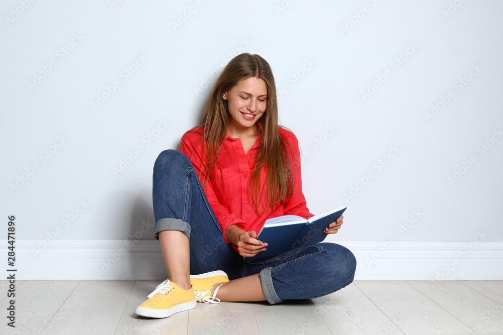Beautiful young woman reading book on wooden floor near light wall Beautiful young woman reading book on wooden floor near light wall
