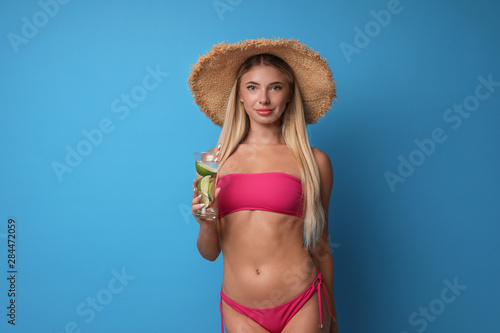Pretty young woman wearing stylish bikini with cocktail on blue background