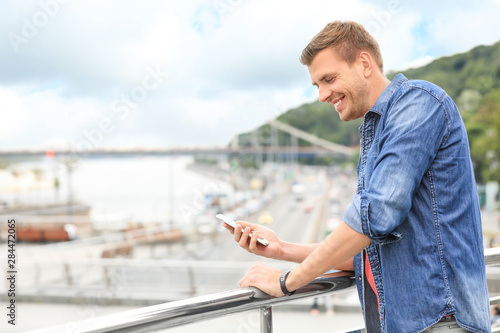 Portrait of handsome man with smartphone on bridge