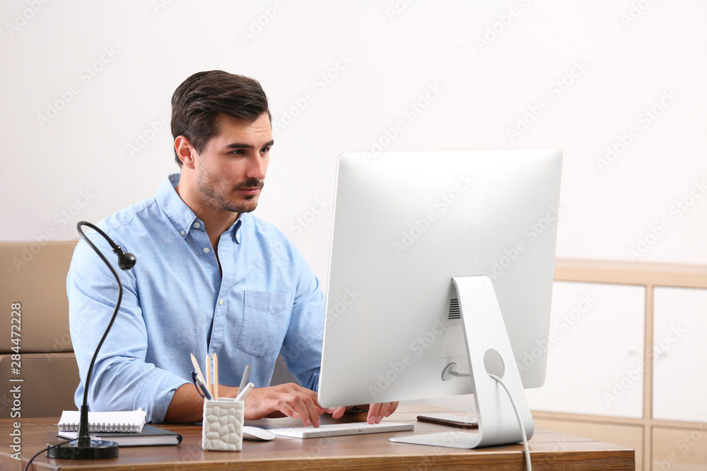 Handsome young man working with computer at table in office Handsome young man working with computer at table in office