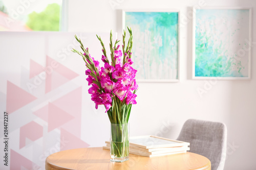 Vase with beautiful pink gladiolus flowers on wooden table in room, space for text