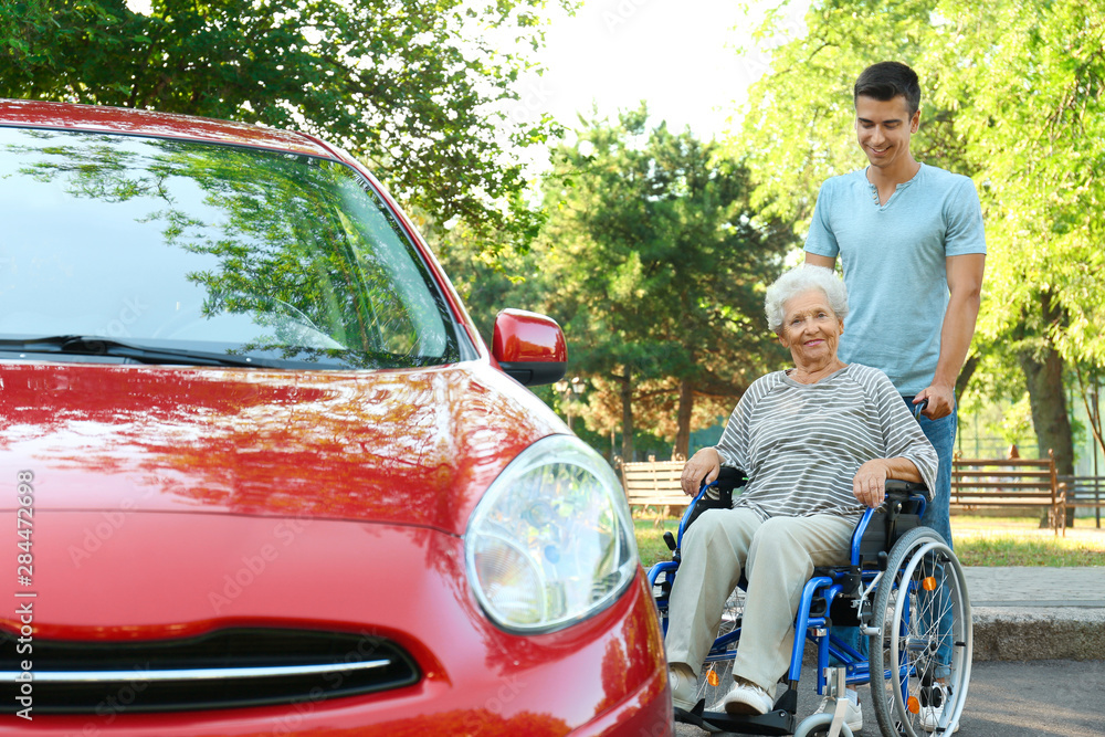 Young man with disabled senior woman in wheelchair near car outdoors