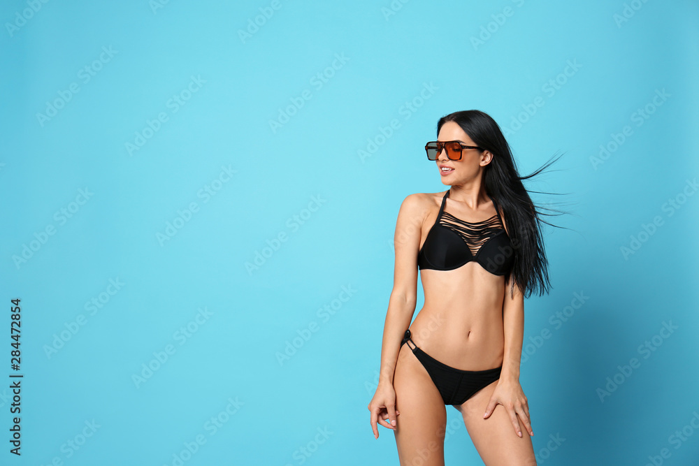 Obraz premium Beautiful young woman in stylish bikini with sunglasses on light blue background. Space for text