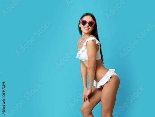 Beautiful young woman in white bikini with sunglasses on light blue background. Space for text © New Africa