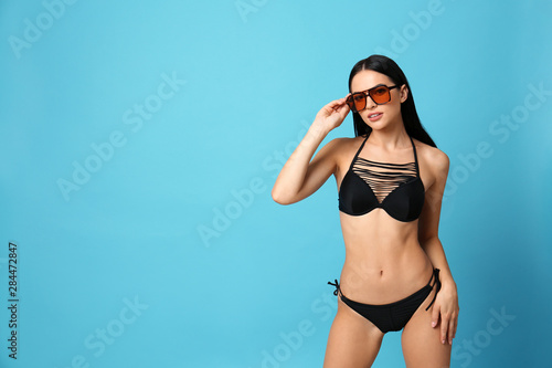 Beautiful young woman in stylish bikini with sunglasses on light blue background. Space for text © New Africa