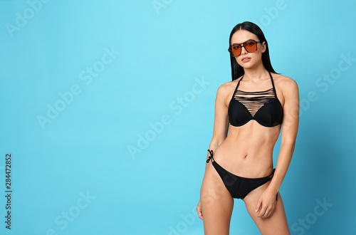 Beautiful young woman in stylish bikini with sunglasses on light blue background. Space for text © New Africa