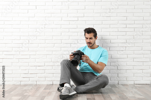 Young photographer with professional camera near brick wall. Space for text